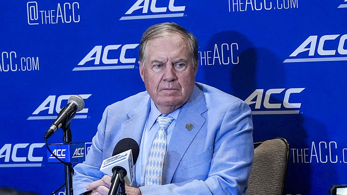 North Carolina head coach William Belichick sits at a table with microphones in front of an ACC backdrop.