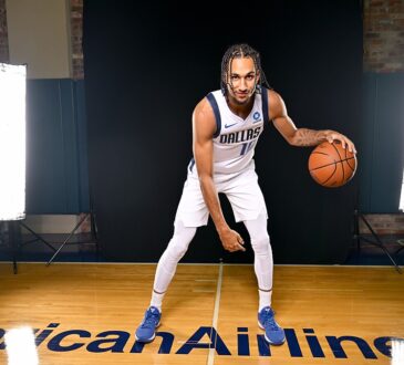 Dallas Mavericks guard Zaccharie Risacher crouches in a dribbling pose with a basketball in front of a black studio backdrop.