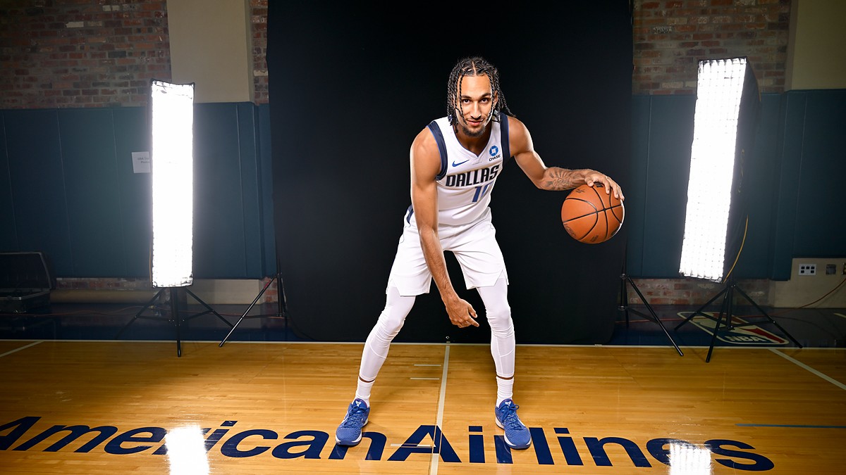 Dallas Mavericks guard Zaccharie Risacher crouches in a dribbling pose with a basketball in front of a black studio backdrop.