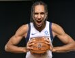 Dallas Mavericks forward Zaccharie Risacher roars toward the camera while gripping a basketball against a black backdrop.