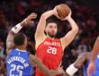 Rockets center Alperen Şengün holds the ball overhead as Mavericks defenders close in.