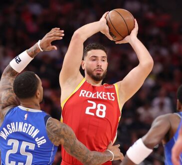 Rockets center Alperen Şengün holds the ball overhead as Mavericks defenders close in.