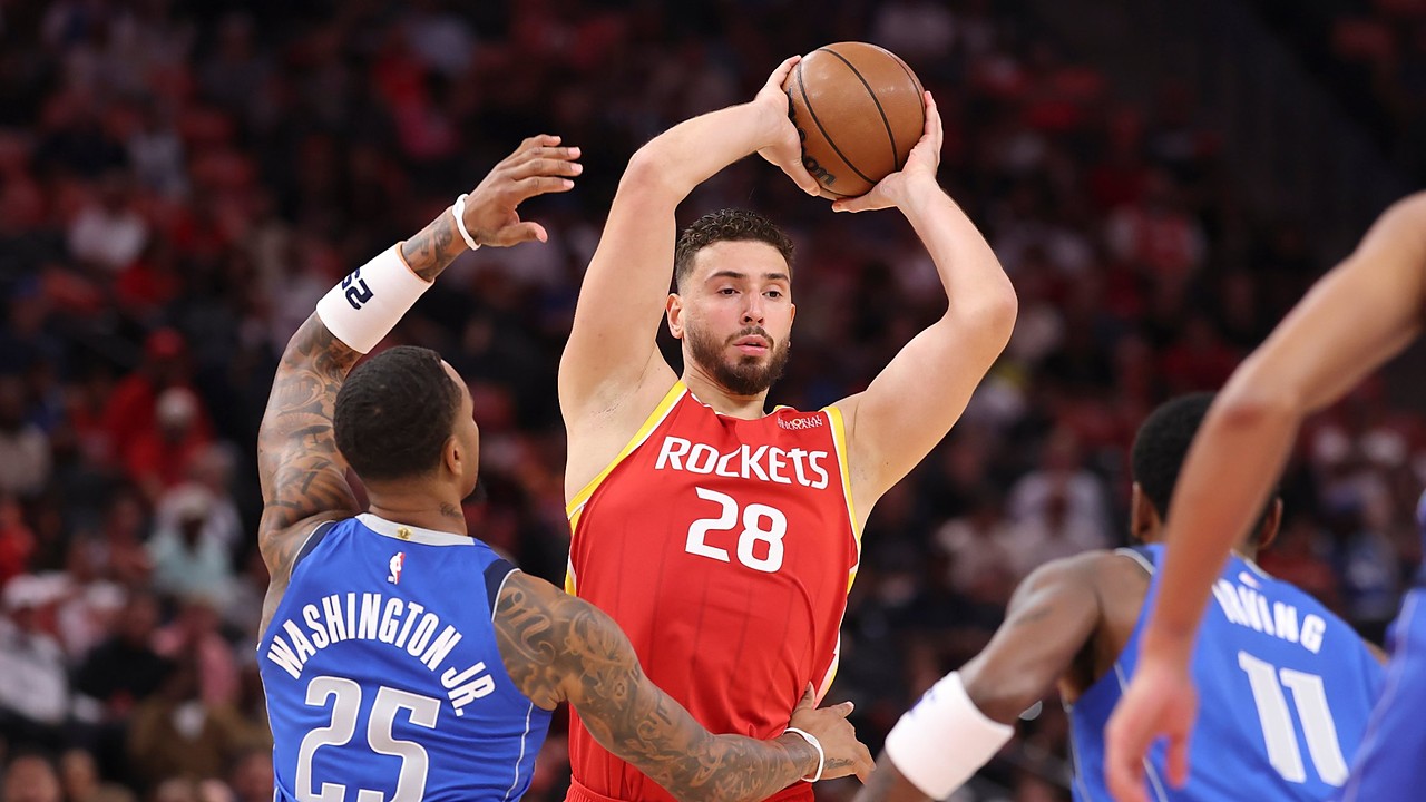 Rockets center Alperen Şengün holds the ball overhead as Mavericks defenders close in.