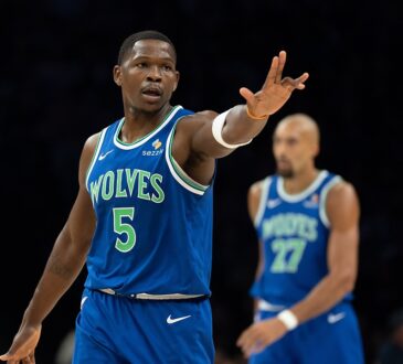 Minnesota Timberwolves guard Anthony Edwards holds up three fingers on each hand after making a shot, with teammates behind him.