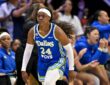 Dallas Wings guard Arike Ogunbowale jogs back upcourt in a blue Dallas jersey as teammates cheer from the bench behind her.