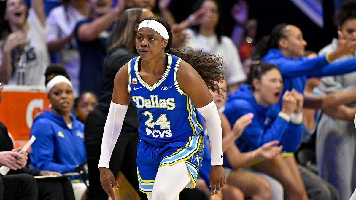 Dallas Wings guard Arike Ogunbowale jogs back upcourt in a blue Dallas jersey as teammates cheer from the bench behind her.