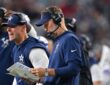 Cowboys head coach Brian Schottenheimer works the sideline in a headset alongside assistant coaches holding a play sheet.