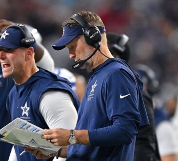 Cowboys head coach Brian Schottenheimer works the sideline in a headset alongside assistant coaches holding a play sheet.