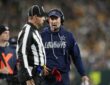 Dallas Cowboys head coach Brian Schottenheimer speaks to an official on the sideline while holding a red flag.
