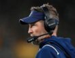 Dallas Cowboys head coach Brian Schottenheimer looks out at the field in profile, wearing a headset and team visor.
