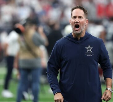 Cowboys head coach Brian Schottenheimer shouts in celebration as he walks off the field holding his cap.