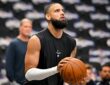 Dallas Mavericks forward Caleb Martin, in a black sleeveless warmup shirt, lines up a shot on an empty-seat backdrop.