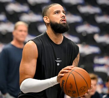 Dallas Mavericks forward Caleb Martin, in a black sleeveless warmup shirt, lines up a shot on an empty-seat backdrop.