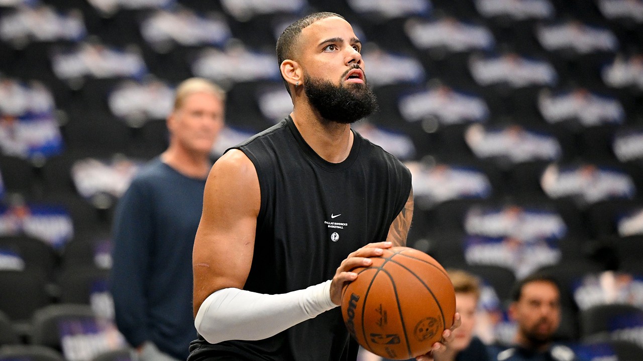 Dallas Mavericks forward Caleb Martin, in a black sleeveless warmup shirt, lines up a shot on an empty-seat backdrop.