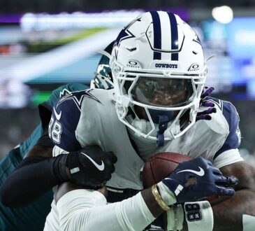 Dallas Cowboys wide receiver CeeDee Lamb secures the ball against his chest as an Eagles cornerback wraps him up from behind.