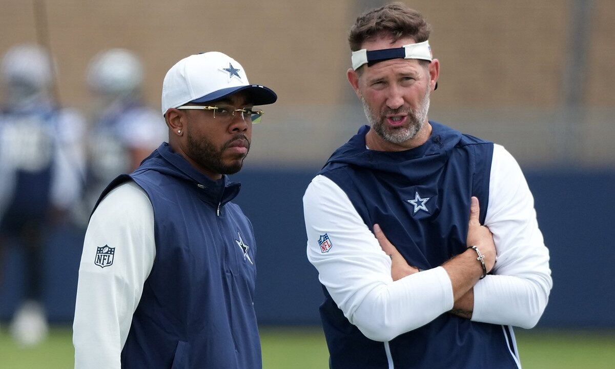 Dallas Cowboys defensive coordinator Christian Parker stands beside head coach Brian Schottenheimer, who talks with arms crossed.
