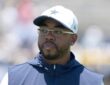 Dallas Cowboys defensive coordinator Christian Parker, in a white team cap and glasses, looks on at practice.