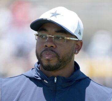 Dallas Cowboys defensive coordinator Christian Parker, in a white team cap and glasses, looks on at practice.