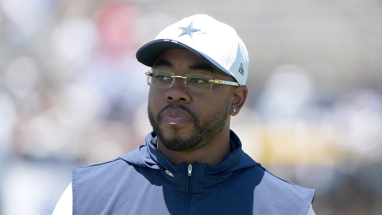 Dallas Cowboys defensive coordinator Christian Parker, in a white team cap and glasses, looks on at practice.