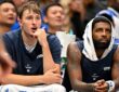 Dallas Mavericks forward Cooper Flagg reacts with his hand at his chin beside guard Kyrie Irving, who wears a towel over his head.
