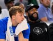 Mavericks forward Cooper Flagg rests his chin on a towel as guard Kyrie Irving laughs beside him on the bench.