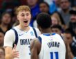 Dallas Mavericks forward Cooper Flagg smiles and reaches toward guard Kyrie Irving, who has his back to the camera.