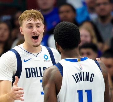 Dallas Mavericks forward Cooper Flagg smiles and reaches toward guard Kyrie Irving, who has his back to the camera.