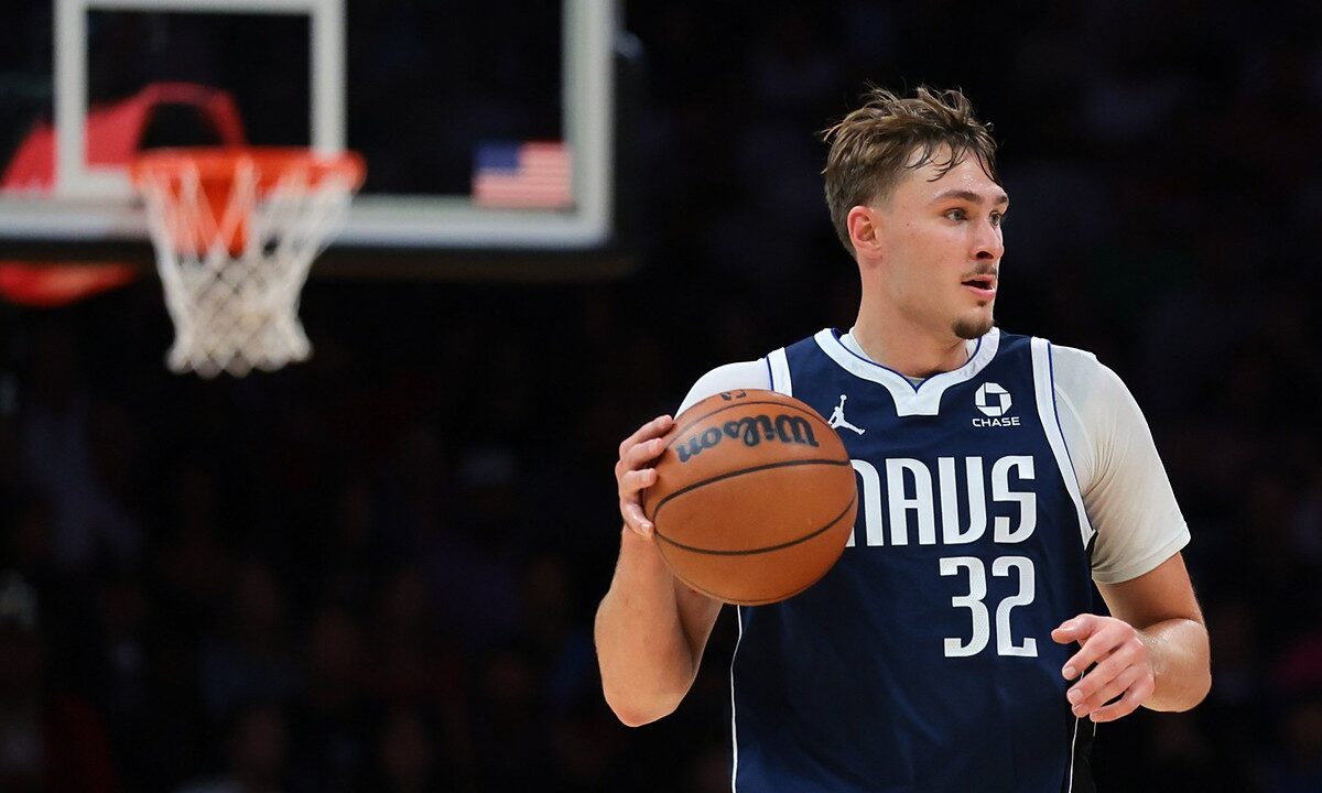Dallas Mavericks forward Cooper Flagg dribbles the ball up the court with a basket blurred in the background.
