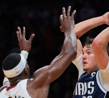 Dallas Mavericks forward Cooper Flagg holds the ball high over his head as Miami Heat center Bam Adebayo reaches up to defend.