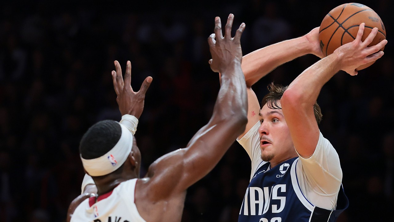 Dallas Mavericks forward Cooper Flagg holds the ball high over his head as Miami Heat center Bam Adebayo reaches up to defend.