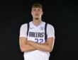 Dallas Mavericks forward Cooper Flagg stands with his arms crossed in a white Dallas jersey against a black backdrop.