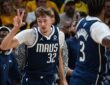 Dallas Mavericks forward Cooper Flagg holds up three fingers as he runs back up the court in front of the Mavericks bench.
