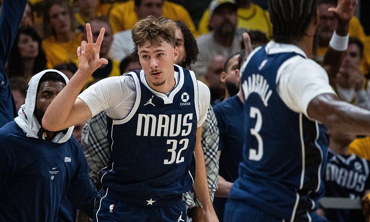Dallas Mavericks forward Cooper Flagg holds up three fingers as he runs back up the court in front of the Mavericks bench.