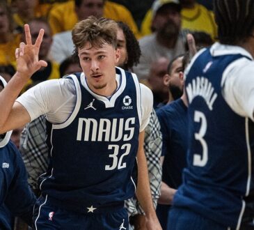 Dallas Mavericks forward Cooper Flagg holds up three fingers as he runs back up the court in front of the Mavericks bench.