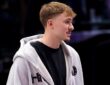 Dallas Mavericks forward Cooper Flagg stands courtside in a gray zip-up hoodie over a black T-shirt.