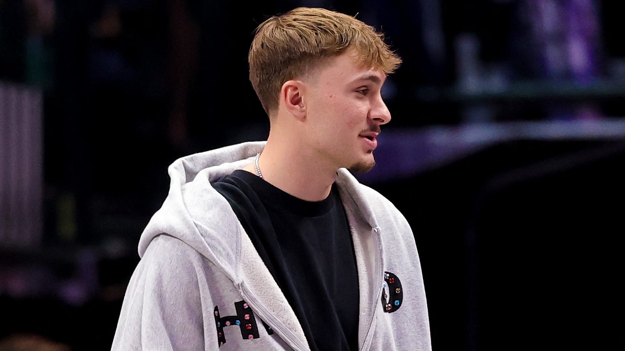 Dallas Mavericks forward Cooper Flagg stands courtside in a gray zip-up hoodie over a black T-shirt.