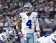 Dallas Cowboys quarterback Dak Prescott shouts at the line of scrimmage with a hand on his hip as linemen settle into stances.