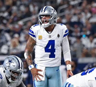 Dallas Cowboys quarterback Dak Prescott shouts at the line of scrimmage with a hand on his hip as linemen settle into stances.