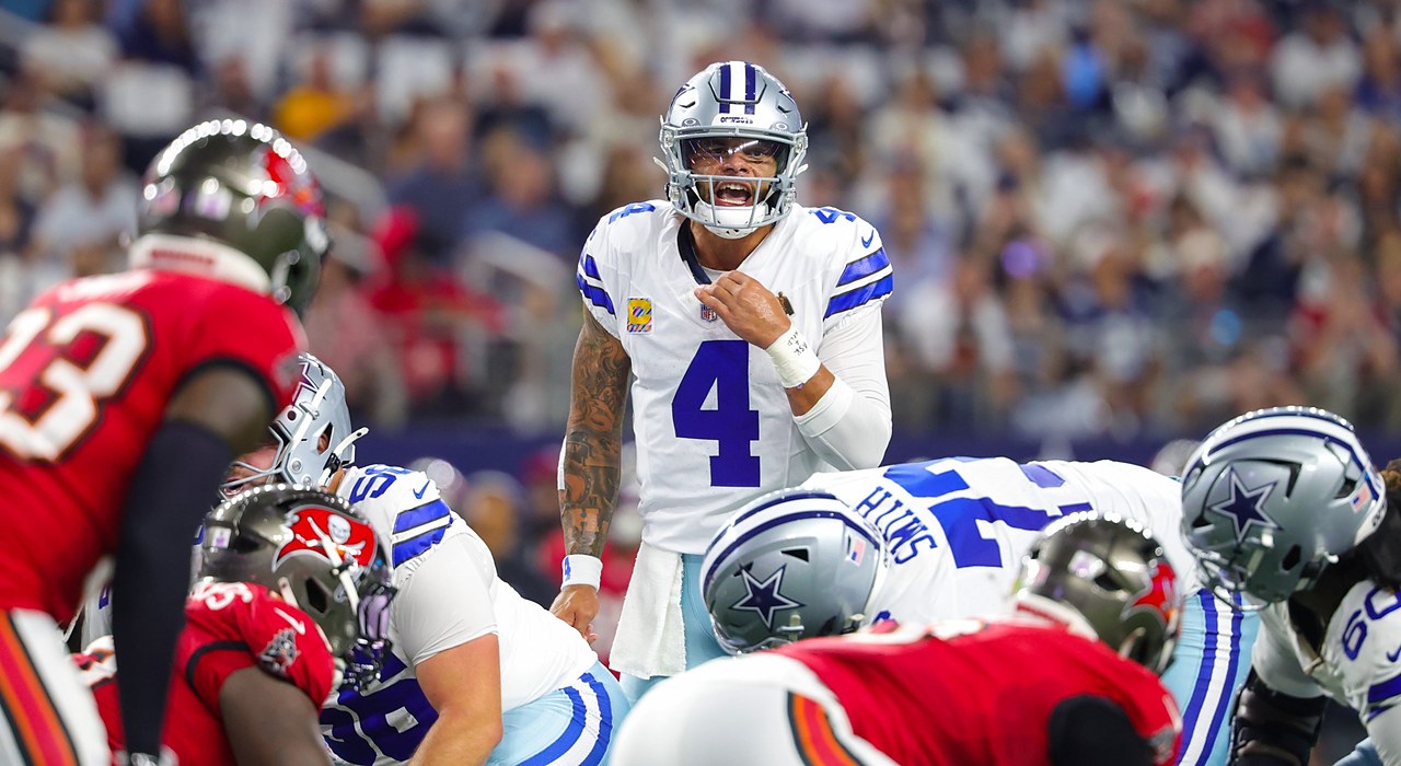 Cowboys quarterback Dak Prescott shouts signals behind the line of scrimmage as linemen crouch in their stances.