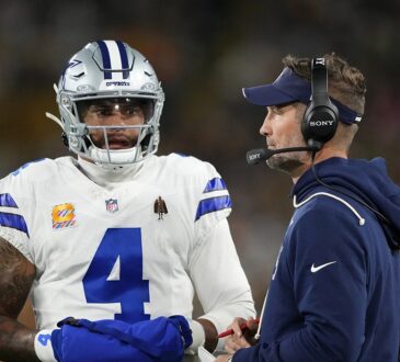 Dallas Cowboys quarterback Dak Prescott talks with head coach Brian Schottenheimer, who wears a headset, on the sideline.
