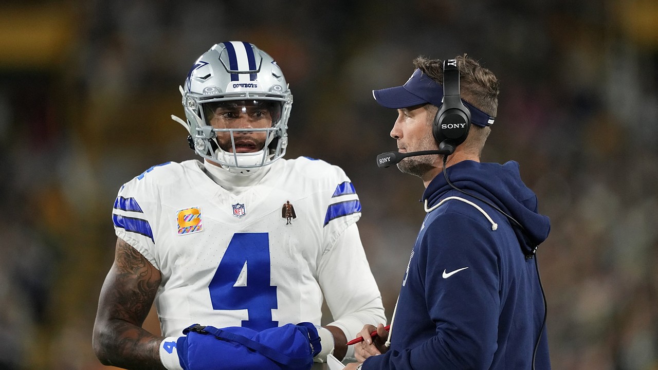 Dallas Cowboys quarterback Dak Prescott talks with head coach Brian Schottenheimer, who wears a headset, on the sideline.