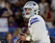 Dallas Cowboys quarterback Dak Prescott holds the ball with both hands while looking downfield.