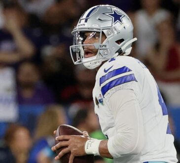 Dallas Cowboys quarterback Dak Prescott holds the ball with both hands while looking downfield.