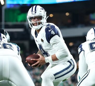 Dallas Cowboys quarterback Dak Prescott turns with the ball in both hands as his offensive linemen block in front of him.