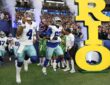 Dallas Cowboys quarterback Dak Prescott and offensive tackle Tyler Guyton run onto the field through smoke past a large Rio sign.