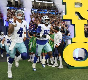 Dallas Cowboys quarterback Dak Prescott and offensive tackle Tyler Guyton run onto the field through smoke past a large Rio sign.
