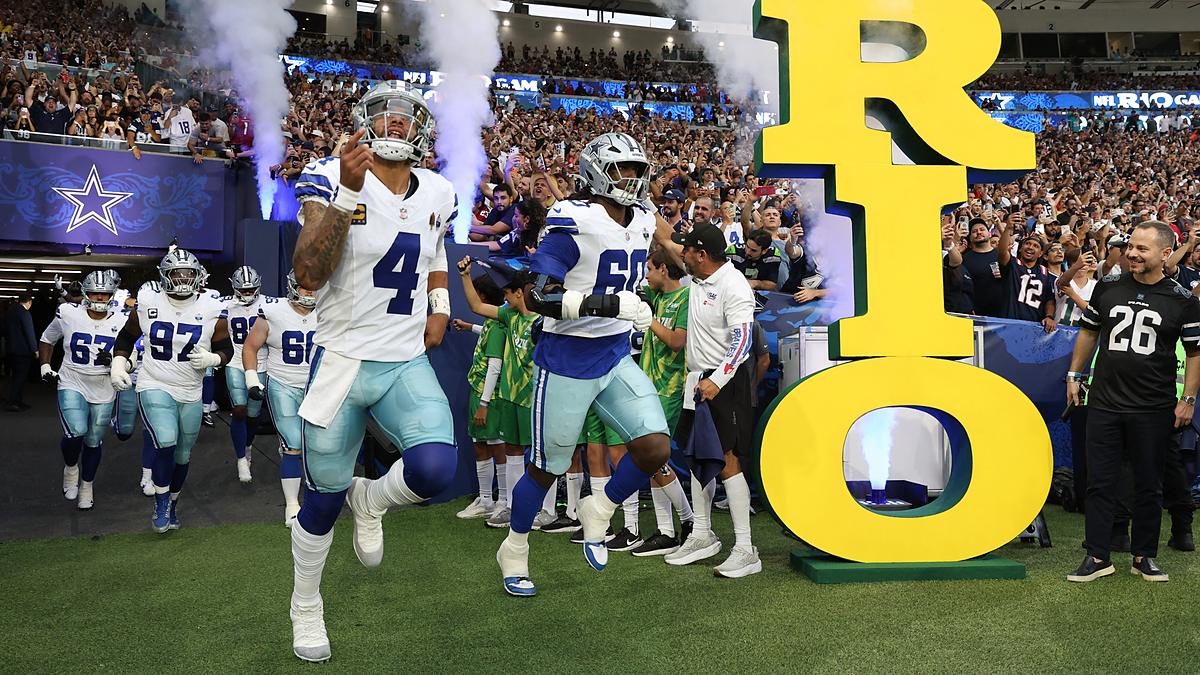 Dallas Cowboys quarterback Dak Prescott and offensive tackle Tyler Guyton run onto the field through smoke past a large Rio sign.