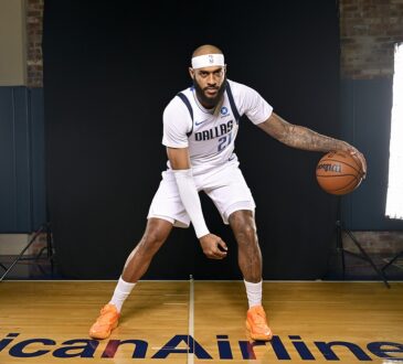 Dallas Mavericks forward/center Daniel Gafford dribbles a basketball in a low stance on the American Airlines Center logo.