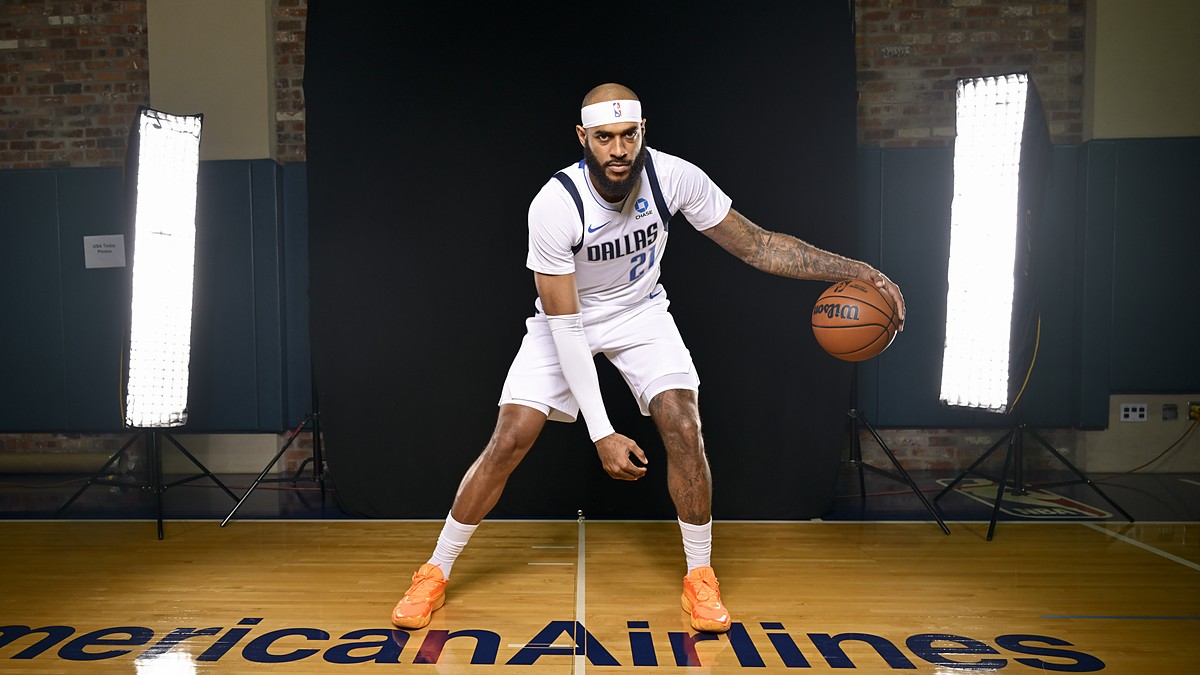 Dallas Mavericks forward/center Daniel Gafford dribbles a basketball in a low stance on the American Airlines Center logo.