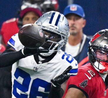 Cowboys cornerback DaRon Bland reaches for the ball with one hand as Buccaneers receiver Emeka Egbuka watches.